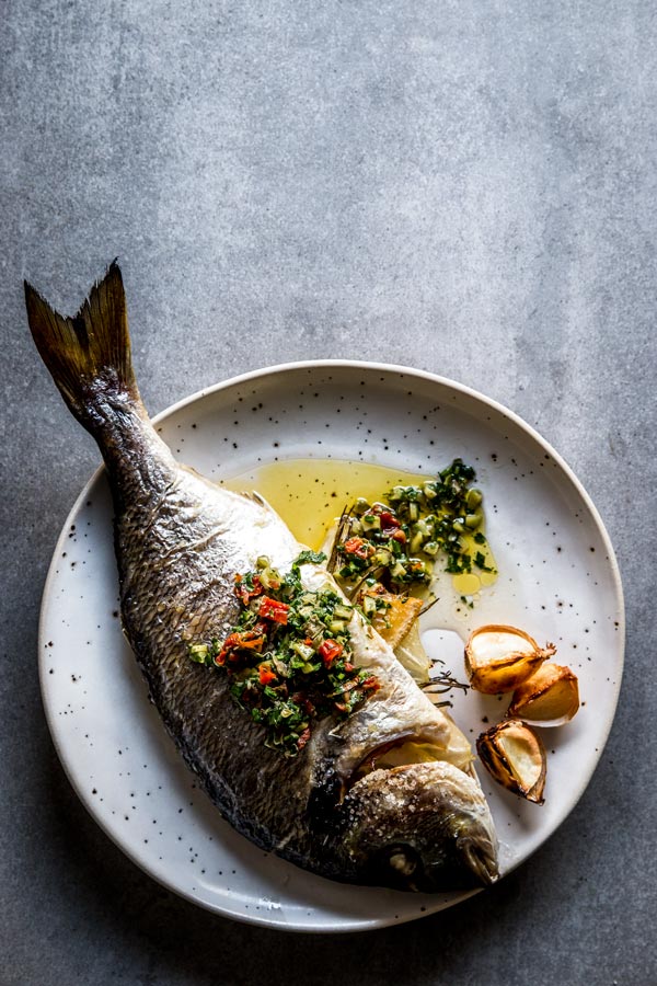 overhead view on baked whole baked fish on white plate with caper salsa