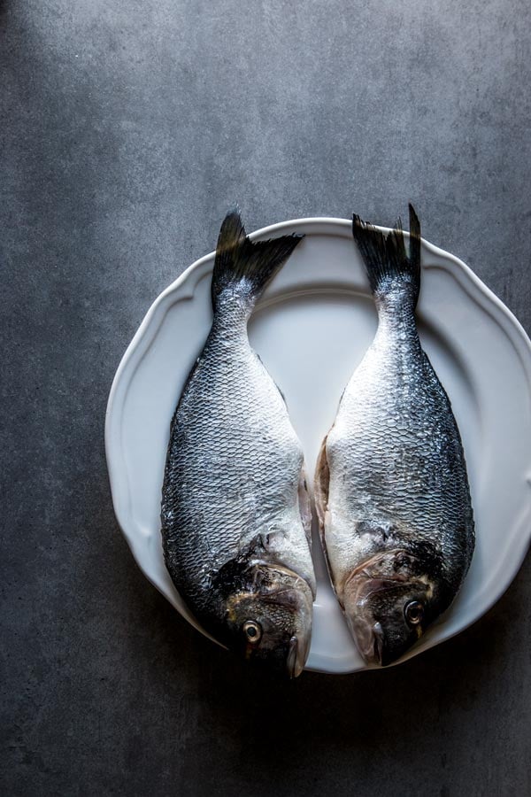 Whole sea bream, gutted and scaled on white plate