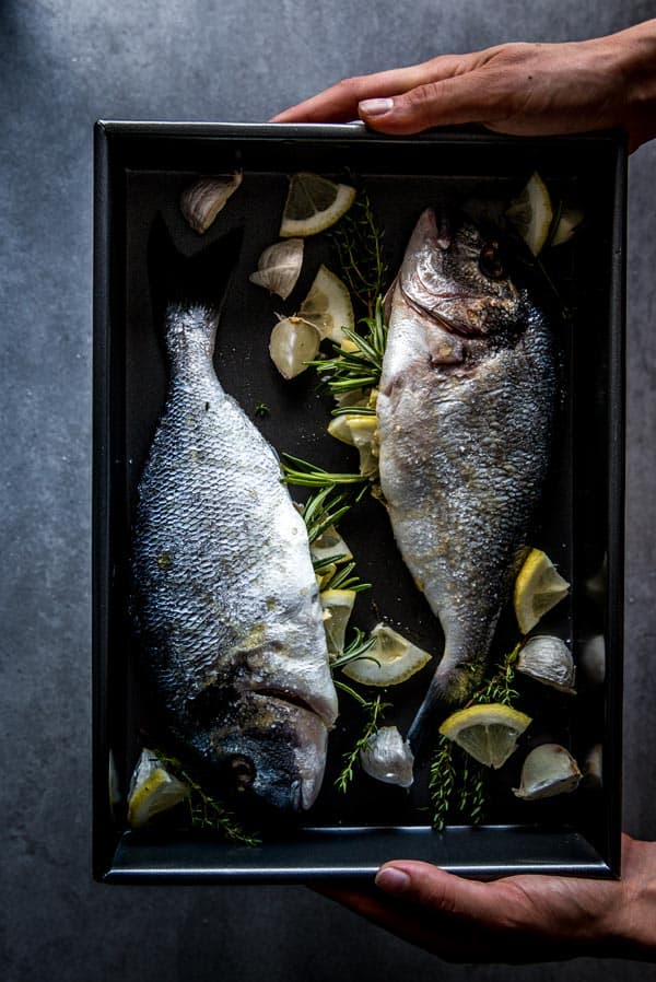 female hands holding black baking tray with unbaked stuffed whole fish