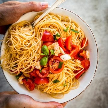 female hands holding plate with caprese pasta