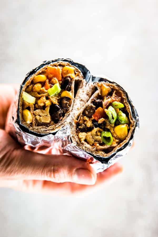 female hand holding breakfast burrito cut in half