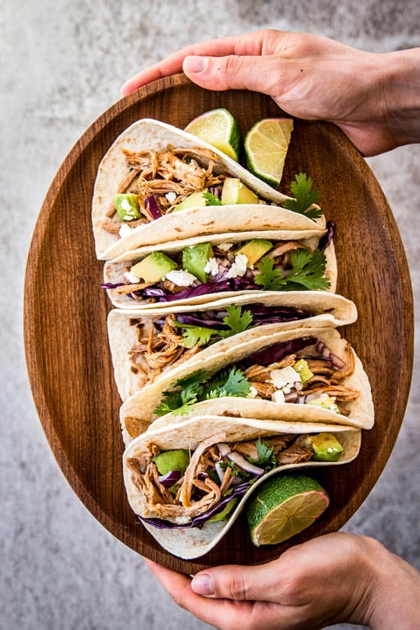 female hands holding pork tacos on wooden platter