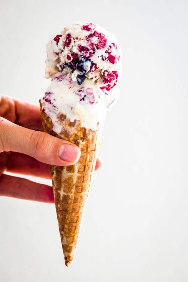 female hand holding cone with scoops of raspberry chocolate chunk ice cream