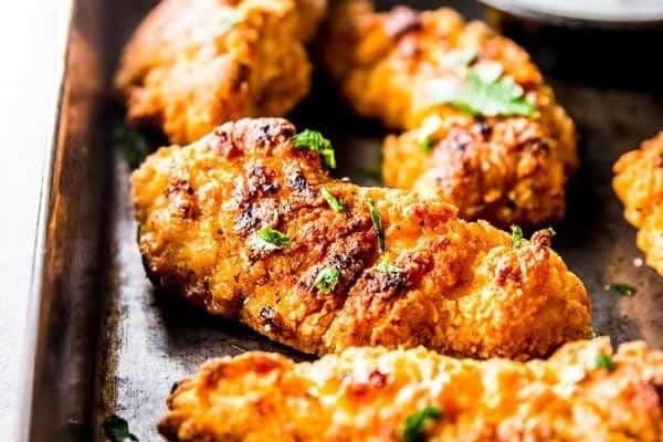 close up photo of garlic parmesan crispy oven fried chicken on a dark sheet pan