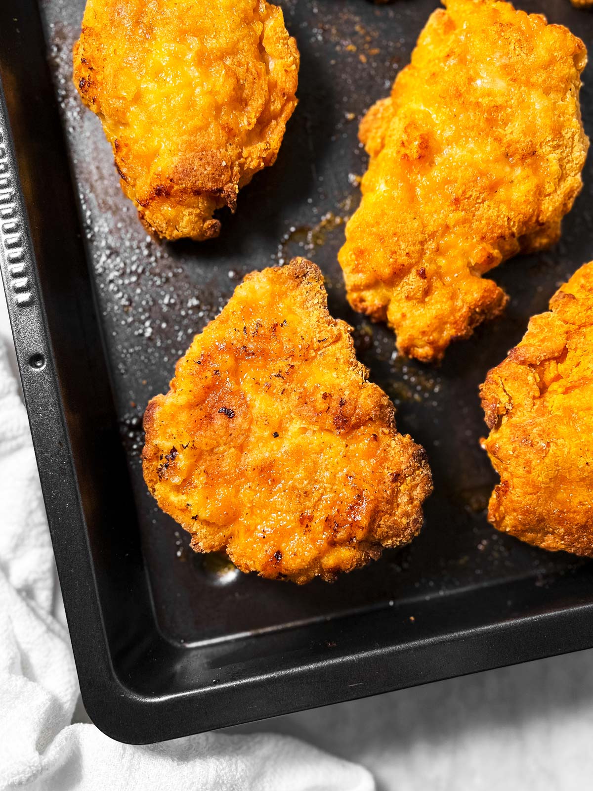 overhead view of garlic parmesan oven fried chicken pieces on black pan