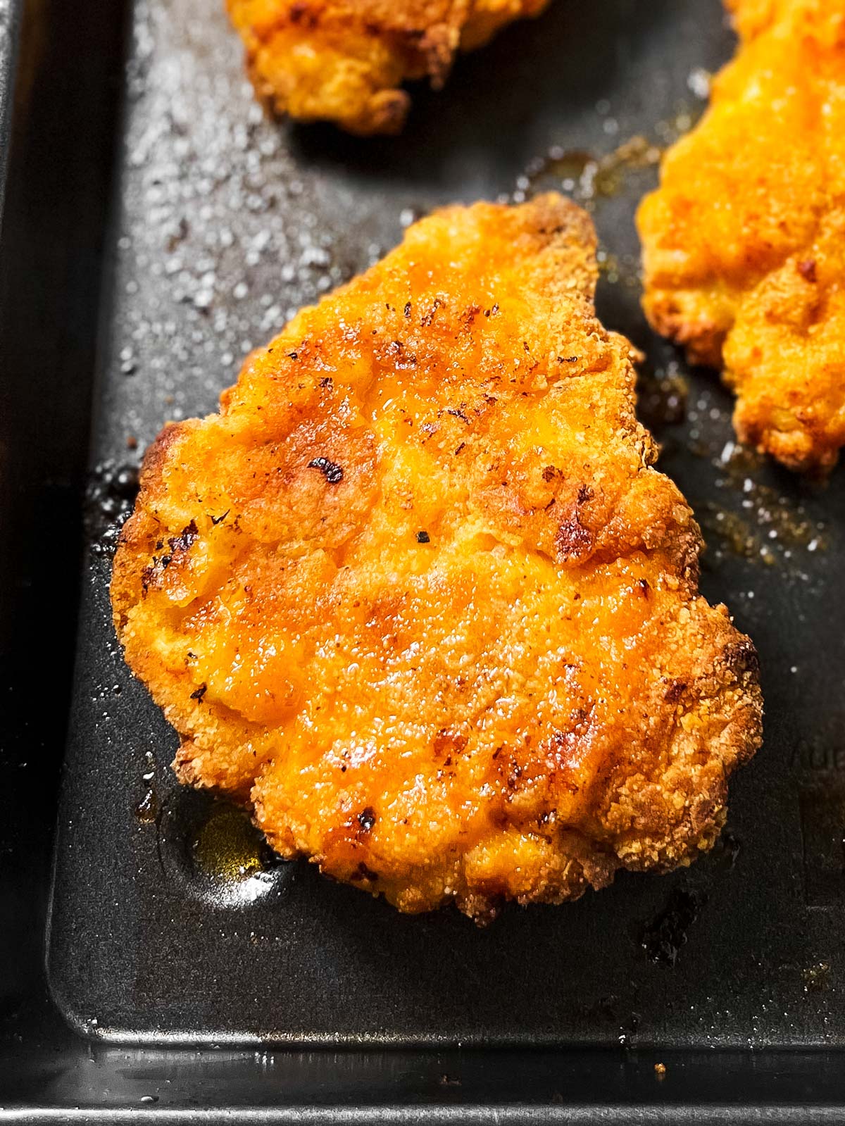 overhead close up view of garlic parmesan oven fried chicken piece on black pan