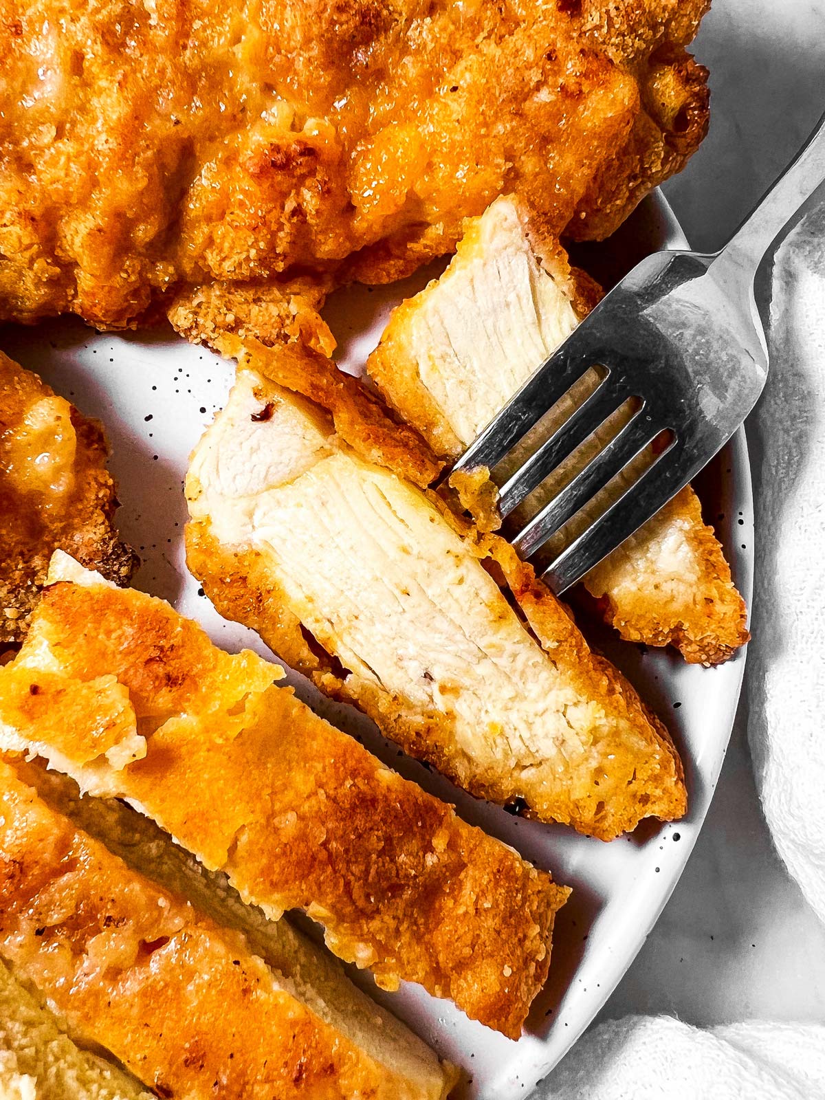 sliced oven fried chicken with fork on white plate