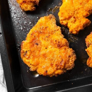 overhead close up view of garlic parmesan oven fried chicken piece on black pan