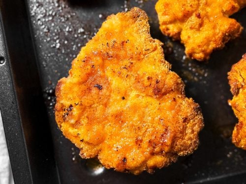 overhead close up view of garlic parmesan oven fried chicken piece on black pan