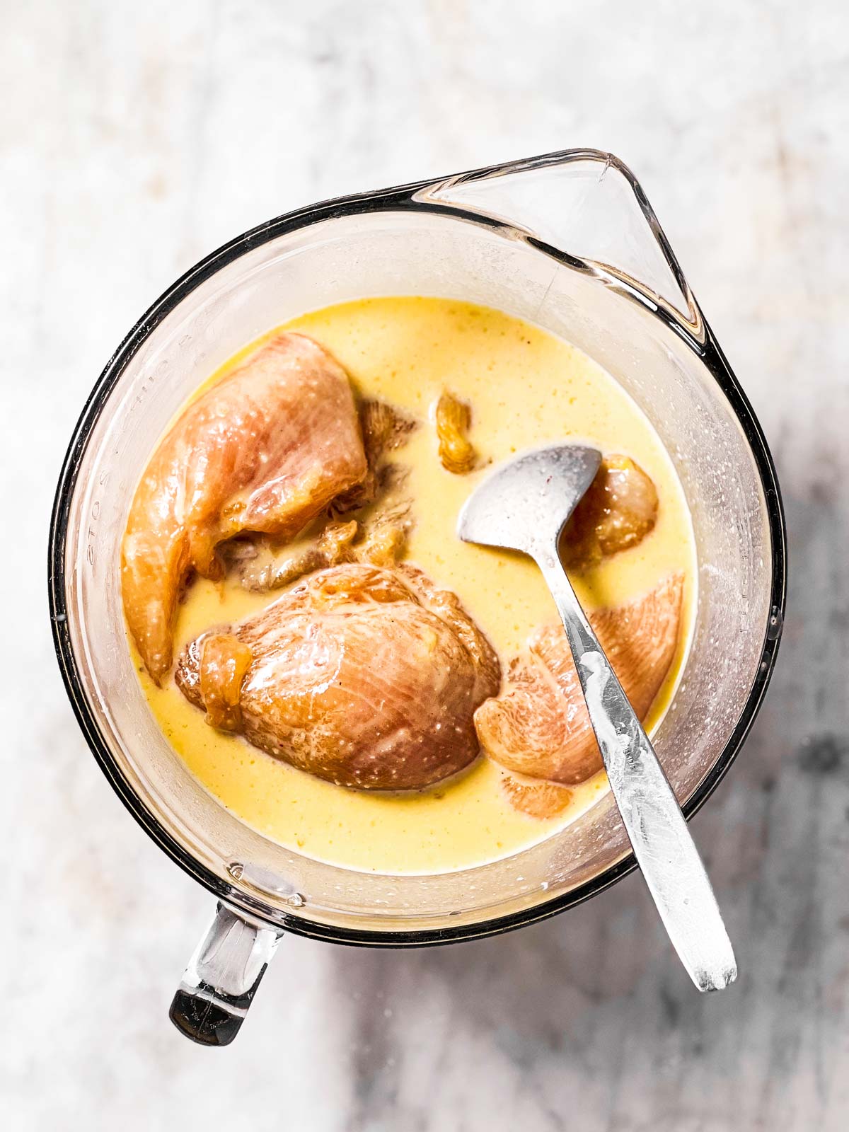 overhead view of chicken  breast pieces in egg wash in glass bowl