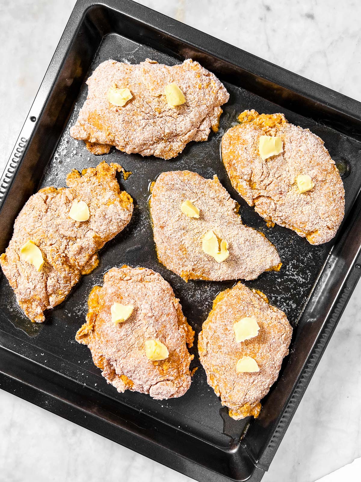 uncooked breaded chicken on black pan