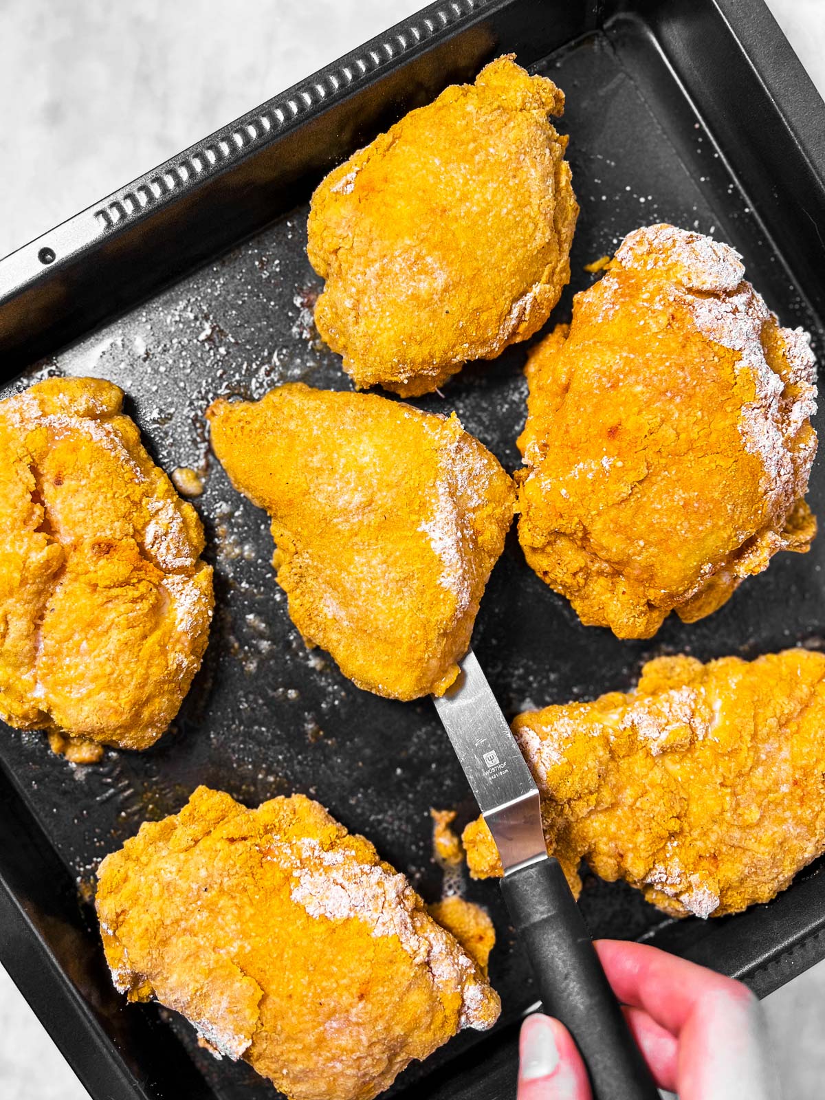 female hand using spatula to flip breaded chicken on black pan