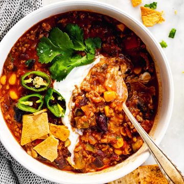 white bowl with crockpot chili and toppings surrounded by tortilla chips