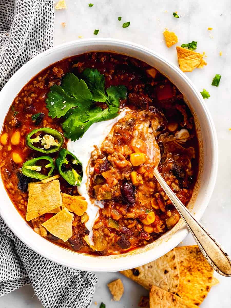 white bowl with crockpot chili and toppings surrounded by tortilla chips