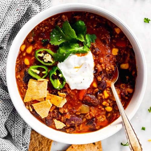 overhead view of white bowl with crockpot chili and toppings