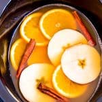 crockpot filled with apple cider, orange slices, apple slices and cinnamon sticks