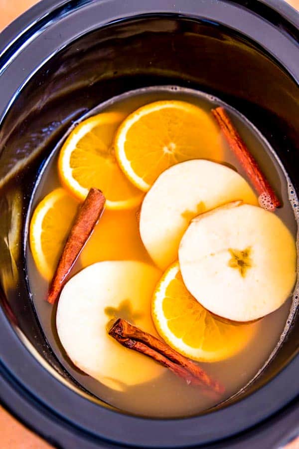 crockpot filled with apple cider, orange slices, apple slices and cinnamon sticks