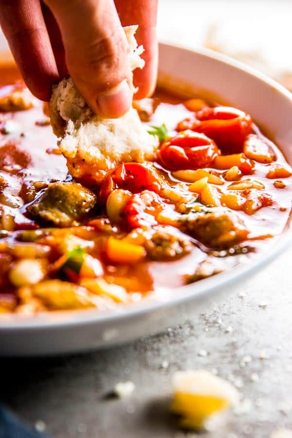 dipping bread into a plate filled with tuscan sausage and white bean soup