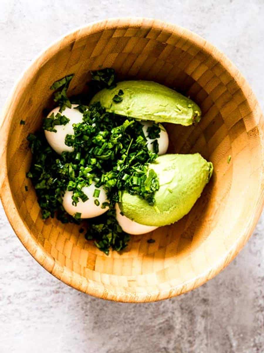 overhead view of wooden bowl with ingredients for avocado egg salad