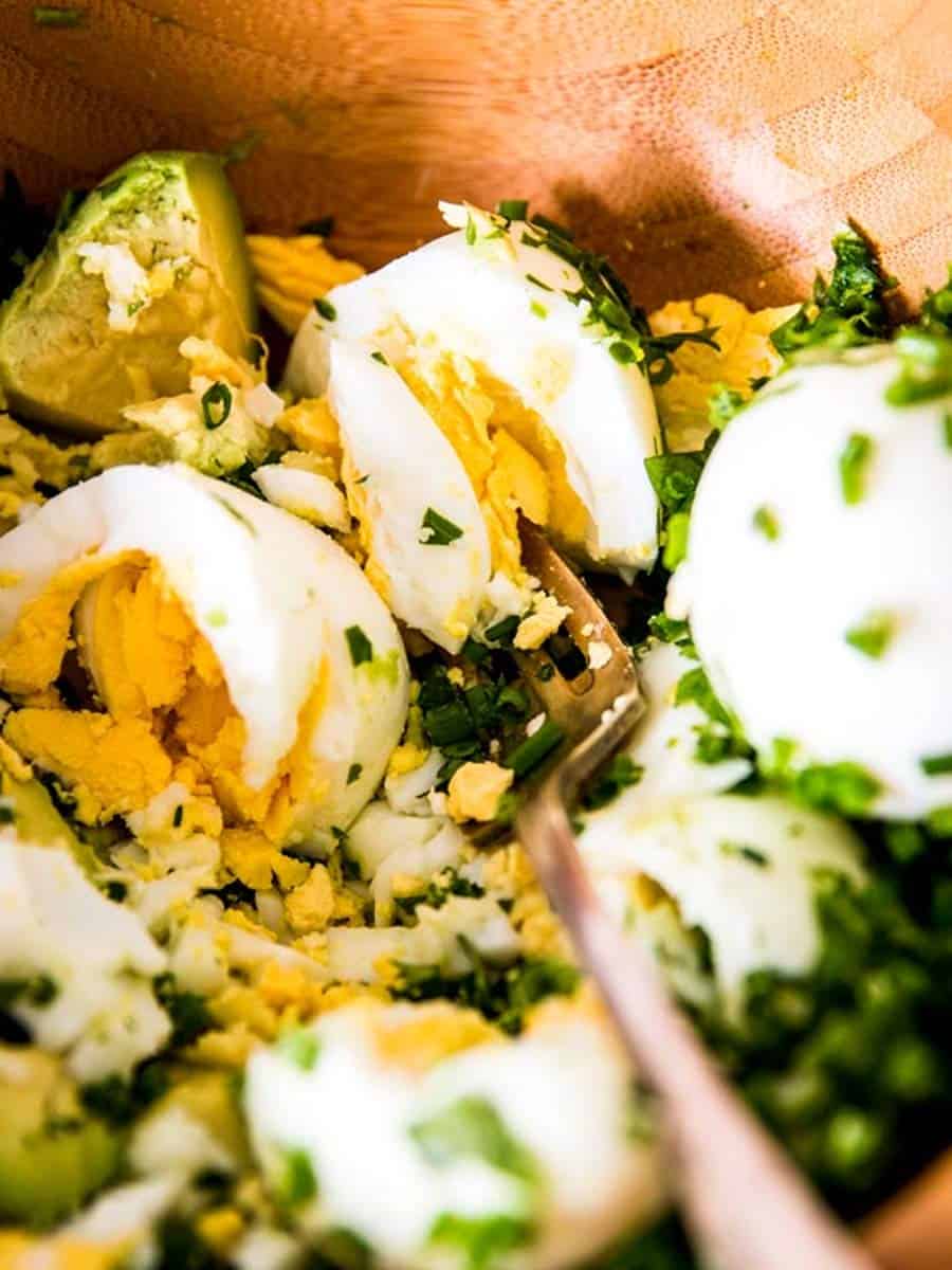 close up photo of fork mashing eggs and avocados