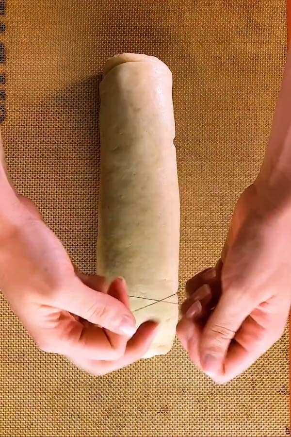 cutting a log of dough into cinnamon rolls with a pice of string - 2
