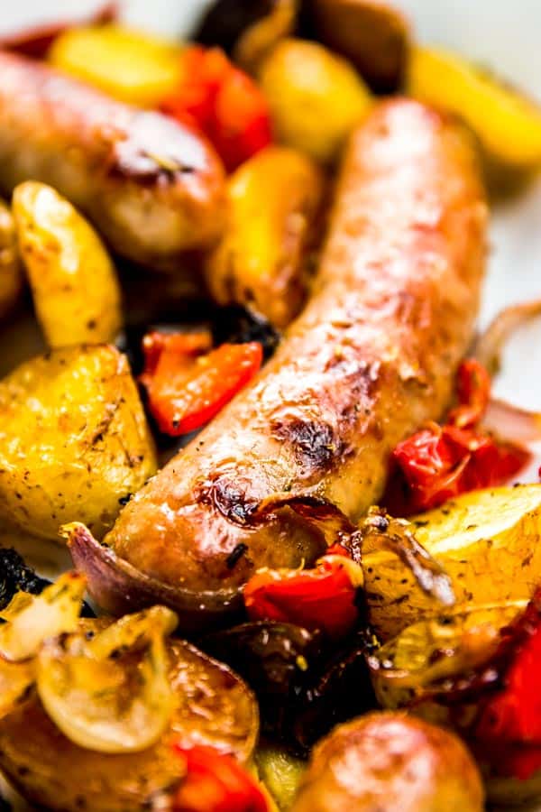 close up of bratwurst surrounded by roasted potatoes and peppers