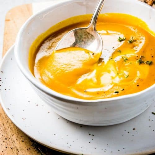 female hand spooning pumpkin soup out of white bowl