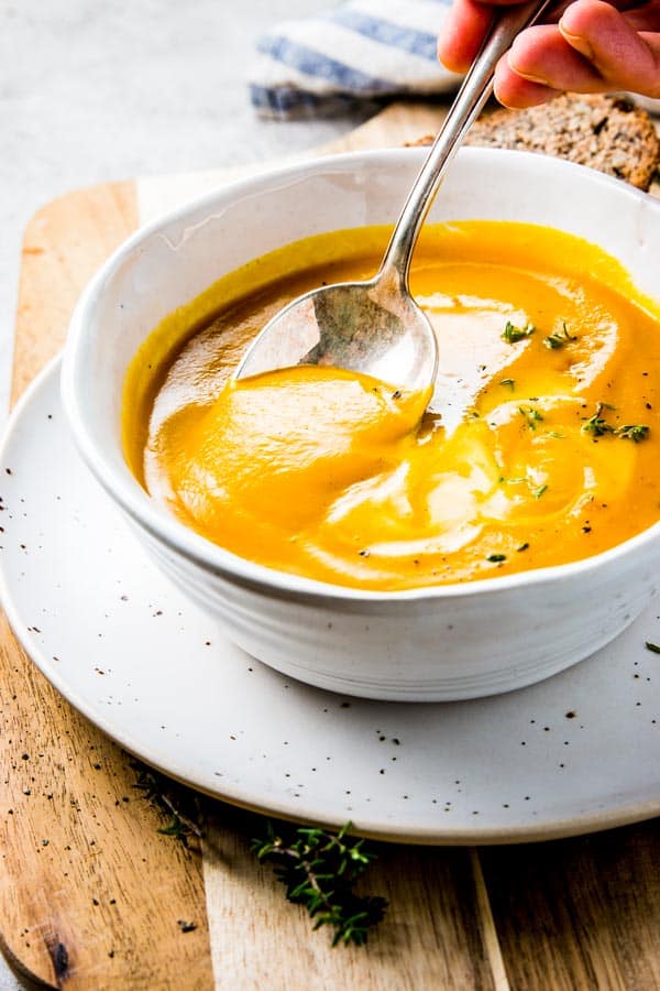 female hand spooning pumpkin soup out of white bowl