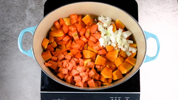 Cut up vegetables for pumpkin soup in a Dutch oven.