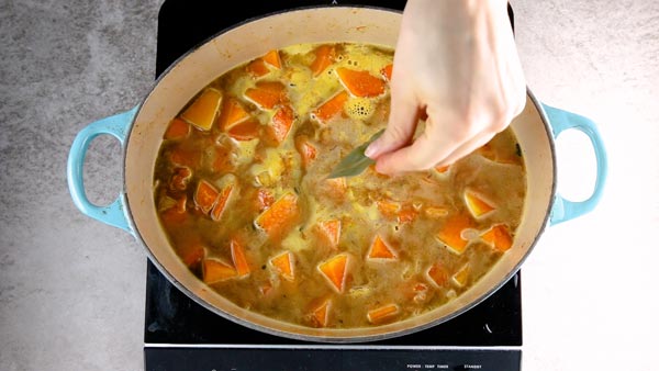 Adding a bay leaf to simmering pumpkin soup.