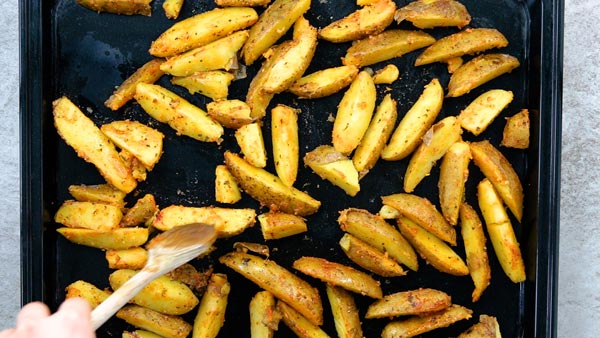 Spreading baked potato wedges on baking sheet