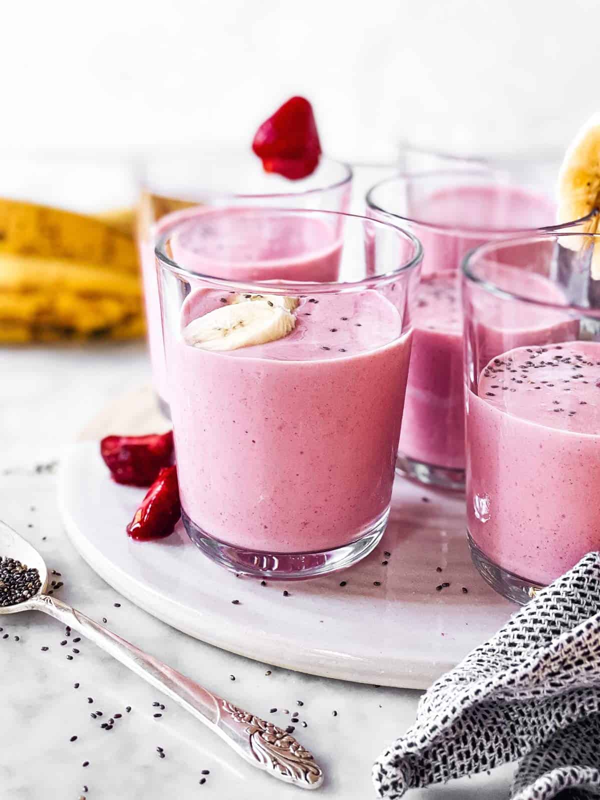 several glasses with strawberry banana smoothie on white platter