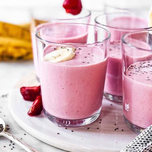 several glasses with strawberry banana smoothie on white platter