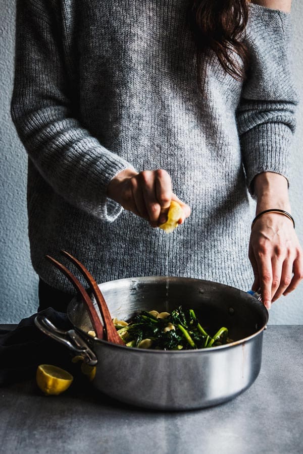 Woman squeezing a lemon over broccoli rabe pasta.