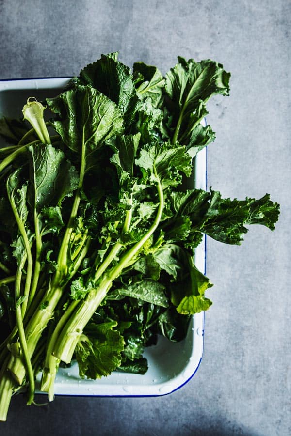 Freshly washed broccoli rabe in an enamel dish.