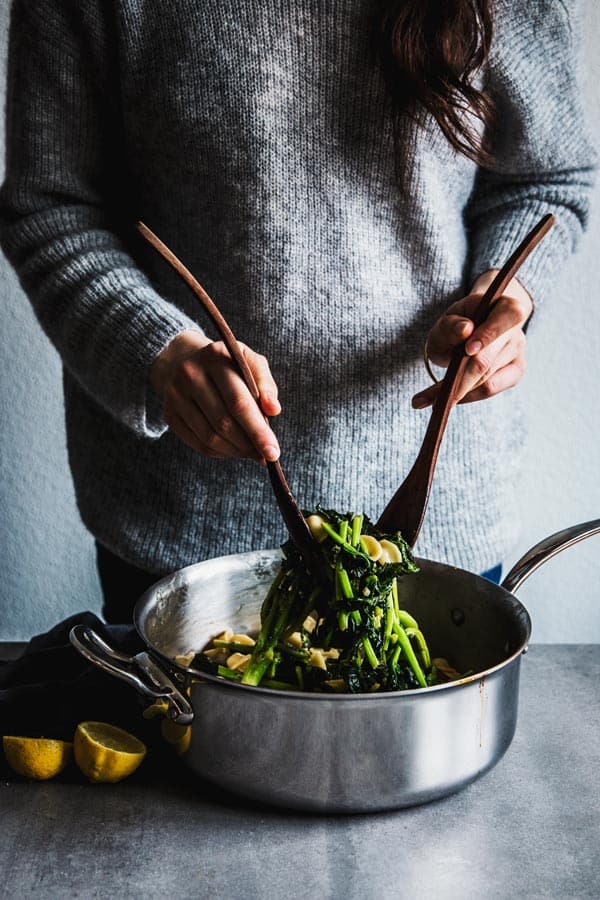 Woman tossing broccoli rabe pasta.