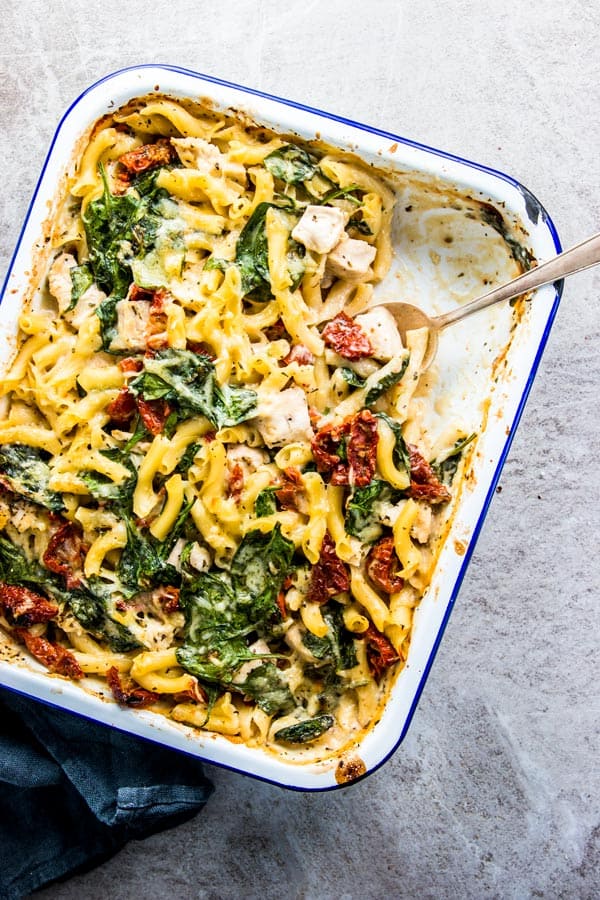 Chicken Florentine Pasta Casserole in a blue rimmed enamel dish with a silver spoon and black linen.