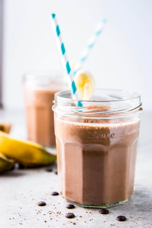 Two glasses of chocolate peanut butter banana smoothie with paper straws