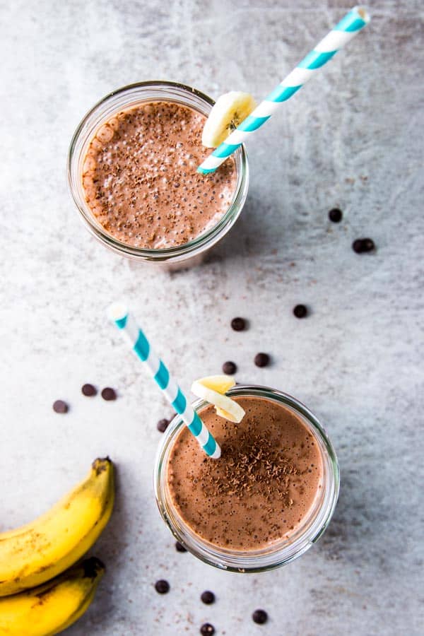 Two glasses of chocolate peanut butter banana smoothie, with bananas and chocolate chips