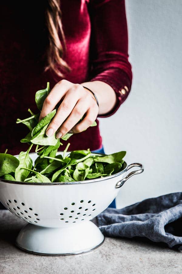 Woman in a red top holding a handful of spinach.