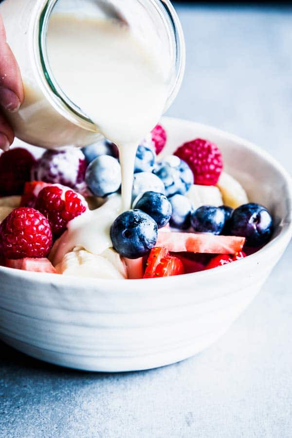 Pouring Greek Yogurt Fruit Salad Dressing over a bowl of triple berry fruit salad.