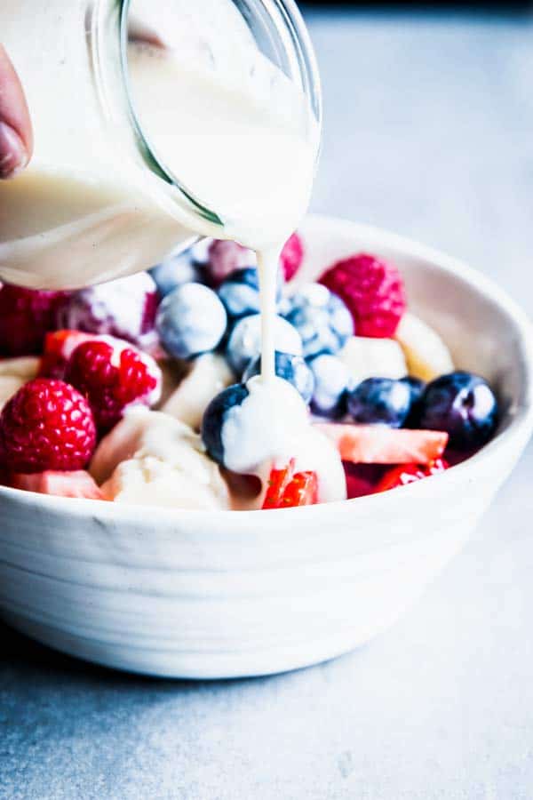 Pouring Greek Yogurt Fruit Salad Dressing over a bowl of triple berry fruit salad.