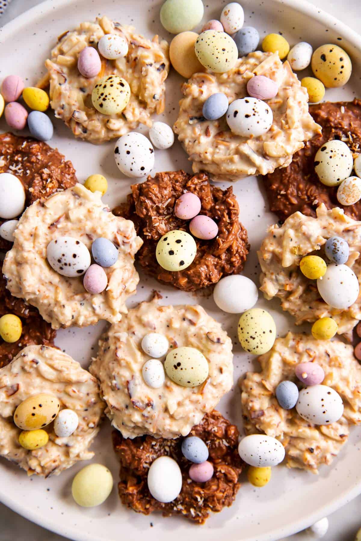 close up photo of several bird's nest cookies and scattered mini eggs on white plate