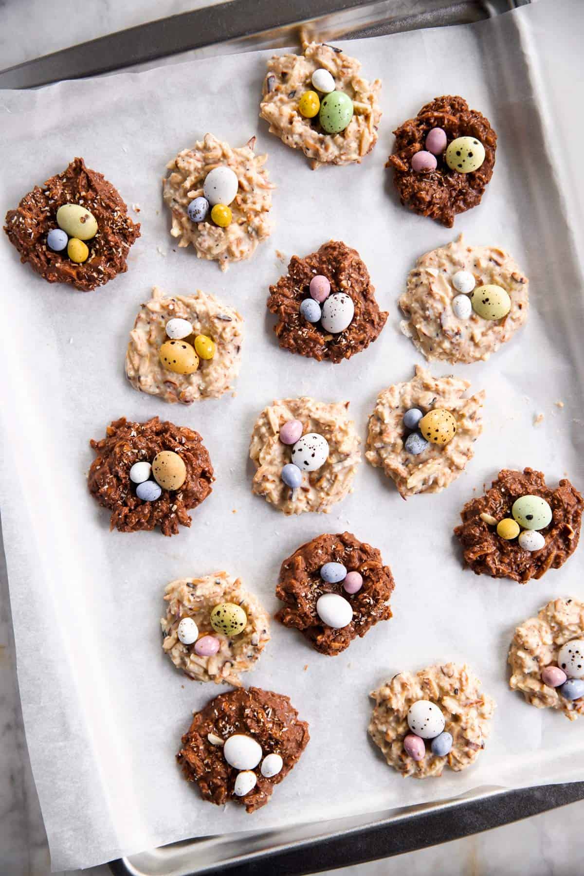 white and brown bird's nest cookies scattered over rimmed sheet pan lined with white baking parchment