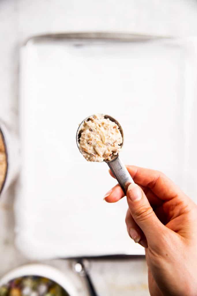 female hand holding tablespoon measure with mixture for bird's nest cookies