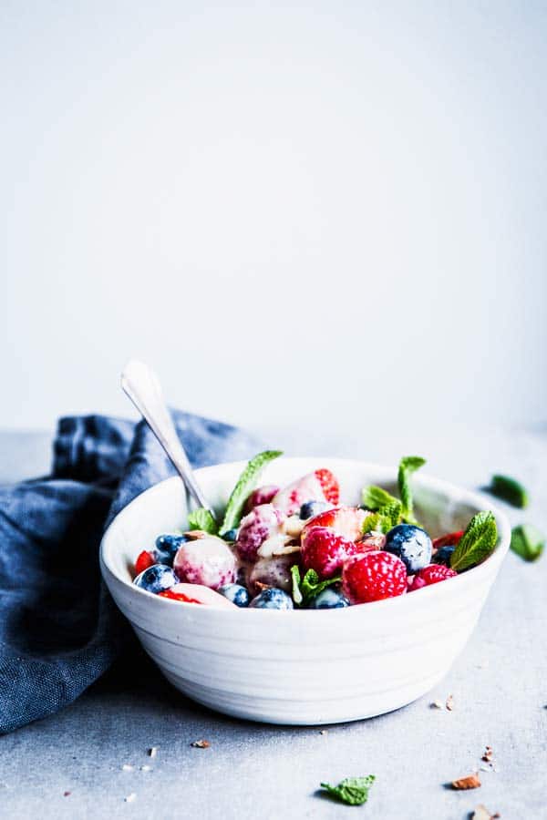 Berry Cheesecake Fruit Salad in a white bowl on the table. Black napkin next to it.