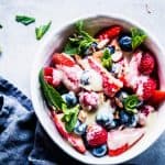 Berry Cheesecake Fruit Salad in a white pottery bowl with a dark napkin and mint sprinkled around.