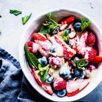 Berry Cheesecake Fruit Salad in a white pottery bowl with a dark napkin and mint sprinkled around.