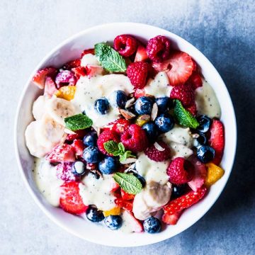 Creamy fruit salad in a white bowl on a light blue surface.