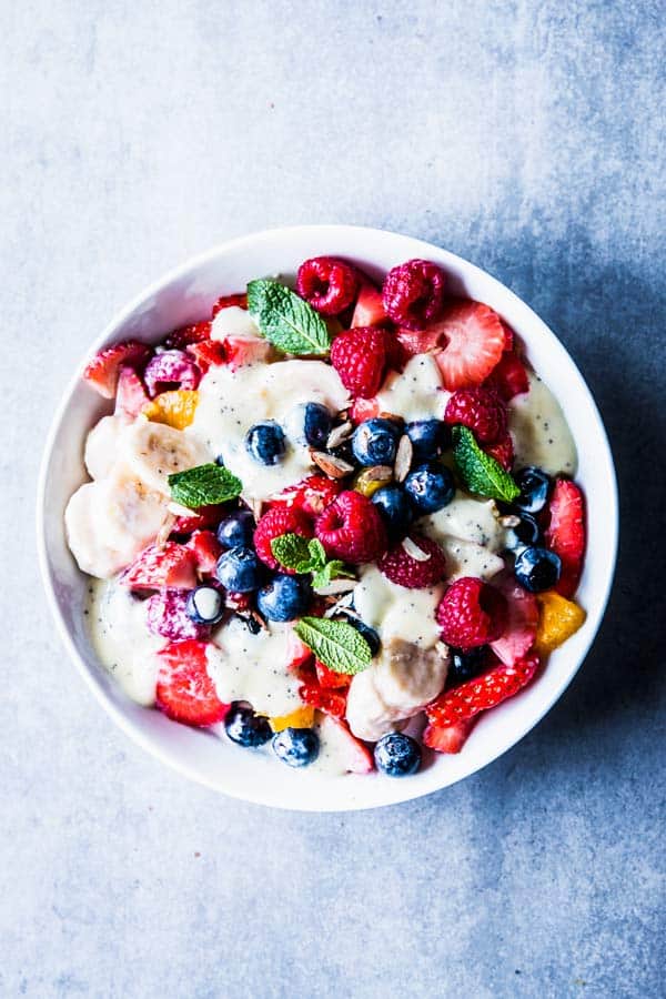 Creamy fruit salad in a white bowl on a light blue surface.